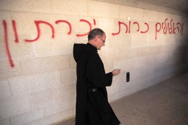 A priest walks past a graffiti reading in Hebrew "idols will be cast out" as he inspects the damage at the Church of the Multiplication at Tabgha, on the shores on the Sea of Galilee in northern Israel, on June 18, 2015, in the aftermath of a suspected arson attack. The suspected attack totally destroyed an external atrium of the Christian shrine, which is believed by many Christians to be the place where Jesus fed the 5,000 in the miracle of the five loaves and two fish, with a church adviser pointing the finger at Jewish extremists. AFP PHOTO / MENAHEM KAHANAMENAHEM KAHANA/AFP/Getty Images