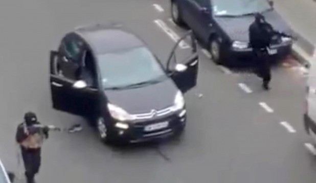 Masked gunman fire their weapons outside the  French satirical newspaper Charlie Hebdo's office, in Paris, Wednesday, Jan. 7, 2015. Paris residents captured chilling video images of two masked gunmen shooting a police officer after an attack at a French satirical newspaper. In the video, the gunmen armed with assault rifles are seen running up to an injured police officer, who lies squirming on the ground. The police officer raises his hands up before one of the assailants shoots him in the head at a close range.  (AP Photo) NO SALES