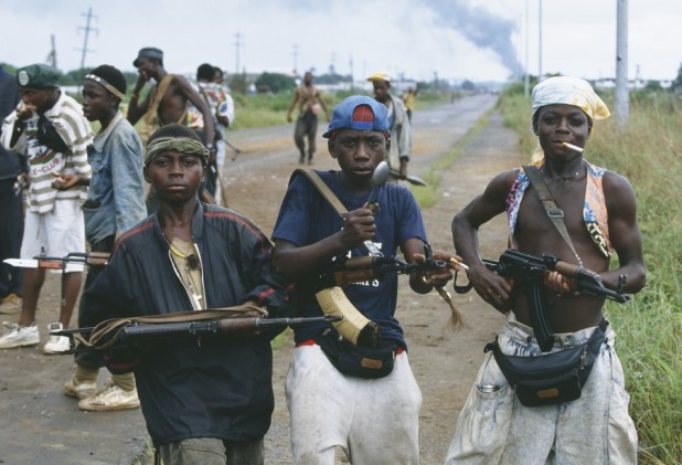 08 Nov 1992, Monrovia, Liberia --- Young rebel fighters pose with their assault rifles in Monrovia during the Liberian Civil War. In 1989, Charles Taylor, leader of the NPFL (National Patriotic Front of Liberia), launched a revolt against the regime of Samuel Doe and continues to fight for control of the country. By the end of 1990, the NPFL controlled 90% of Liberian territory, but not the capital. On June 11, 1991 President Sawyer proposed a peace settlement, to be overseen by a peacekeeping force (ECOMOG) from the Economic Community of West African States (ECOWAS), in which all Liberians would be treated equally. Despite the peace accord, violence among the NPLF, ECOMOG, the AFL alliance, and other factions continued to escalate. Fighting continues for another seven years. --- Image by © Patrick Robert/Sygma/Corbis