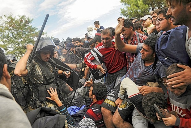 A Macedonian police officer raises his baton toward migrants.