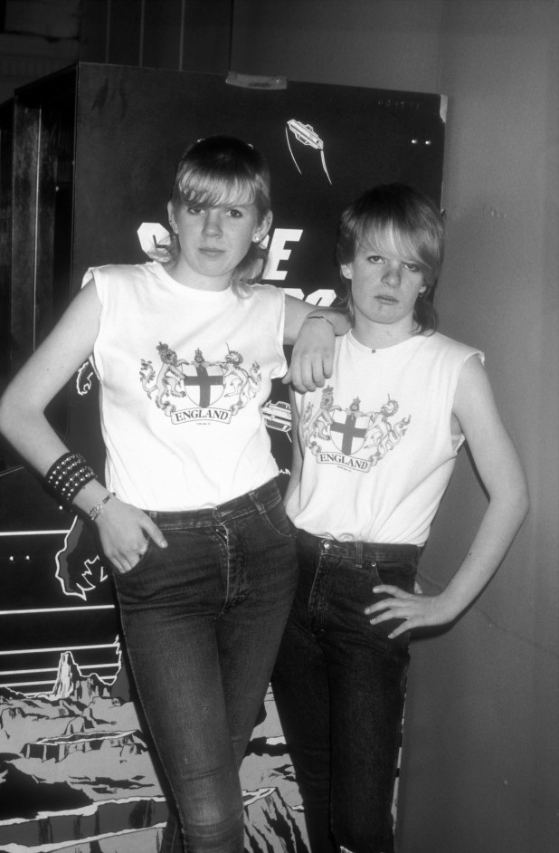 Two skinhead girls, wearing England T shirts, denim, leather bracelet at an arcade in Brighton, UK 1985.