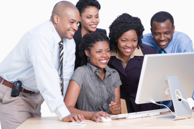 Three young business women and two man looking at computer screen, laughing