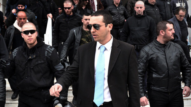 Flanked by his party members, Ilias Kassidiaris (C), an MP and spokesman for the extreme-right Golden Dawn party leaves an appeals court in Athens after his trial on March 7, 2013. The lawmaker from Greece's far right Golden Dawn party has been cleared in court of complicity in an assault and robbery. Kassidiaris was accused of providing the getaway car to five men who attacked a student at a university near Athens with knives and bats and stole his wallet. Kassidiaris shot to notoriety last year when he slapped a left-wing member of parliament in the face and poured a glass of water in the face of another during a television debate ahead of the legislative elections. AFP PHOTO / LOUISA GOULIAMAKI        (Photo credit should read LOUISA GOULIAMAKI/AFP/Getty Images)