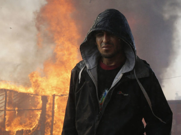 A migrant walks past a burning makeshift shelter in the "Jungle" on the third day of their evacuation and transfer to reception centers in France, as part of the dismantlement of the camp in Calais, France, October 26, 2016. REUTERS/Pascal Rossignol - RTX2QIRQ