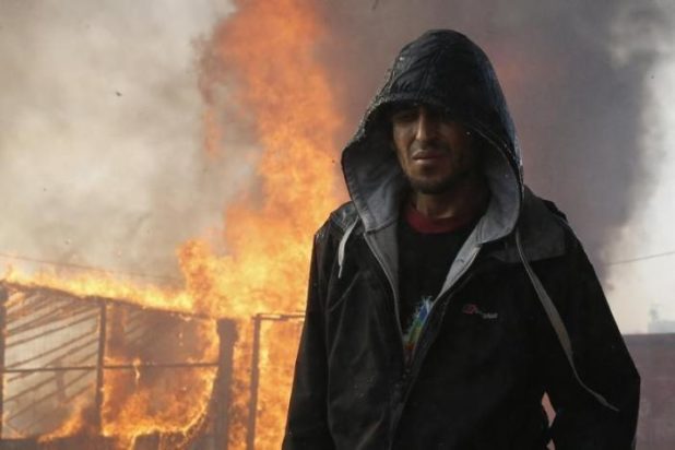 A migrant walks past a burning makeshift shelter in the "Jungle" on the third day of their evacuation and transfer to reception centers in France, as part of the dismantlement of the camp in Calais